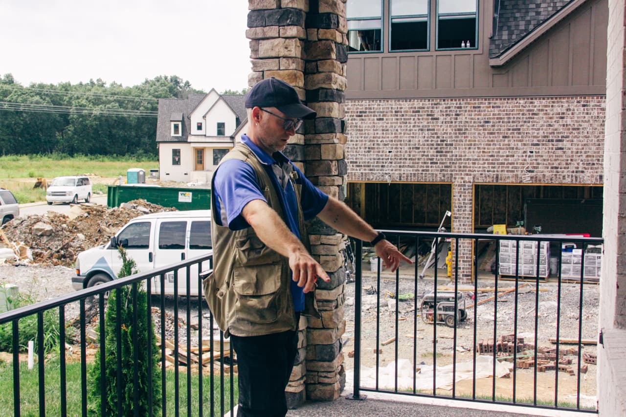 Home inspector standing on a residential balcony during a pre-purchase inspection, visually assessing exterior construction and surrounding areas of the property