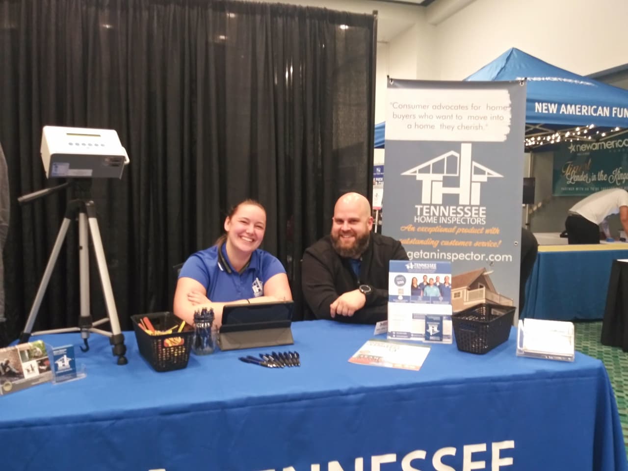 Home inspection team seated at a booth displaying radon testing equipment and informational materials during a radon testing service event